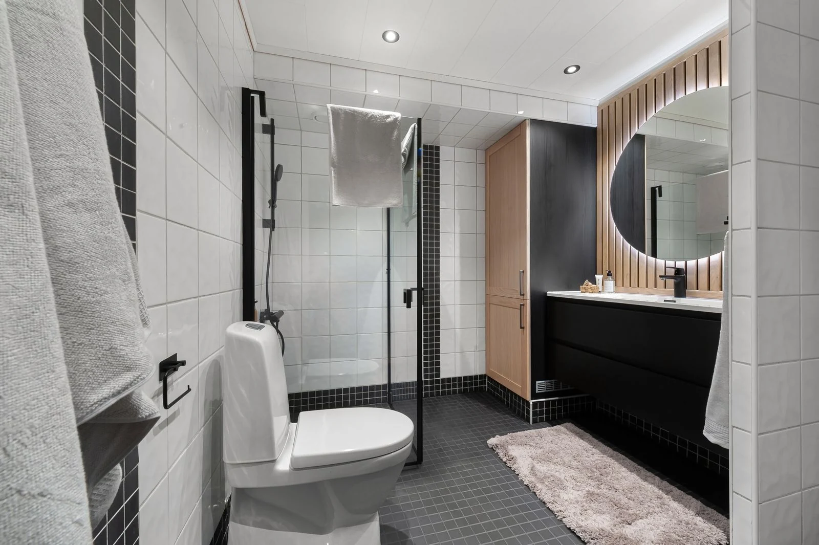 Contemporary bathroom design featuring a clean aesthetic with black and white tiles, a large mirror, and wooden accents