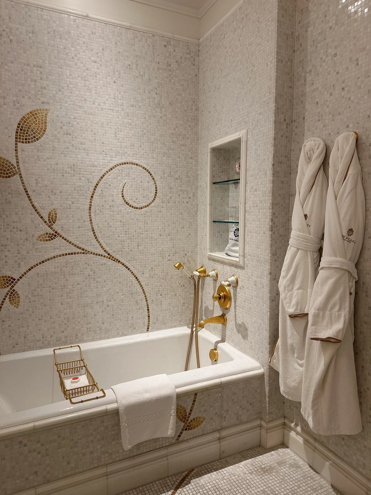 Luxurious bathroom showcasing gold fixtures, mosaic tile, and white robes