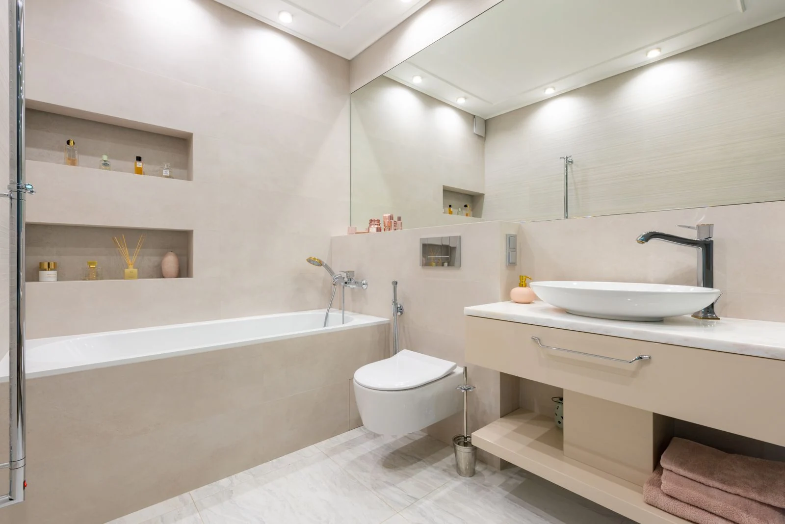 Interior of light modern bathroom with sink and faucet on cabinet with decorative objects next to bathtub and toilet under mirror and shelves