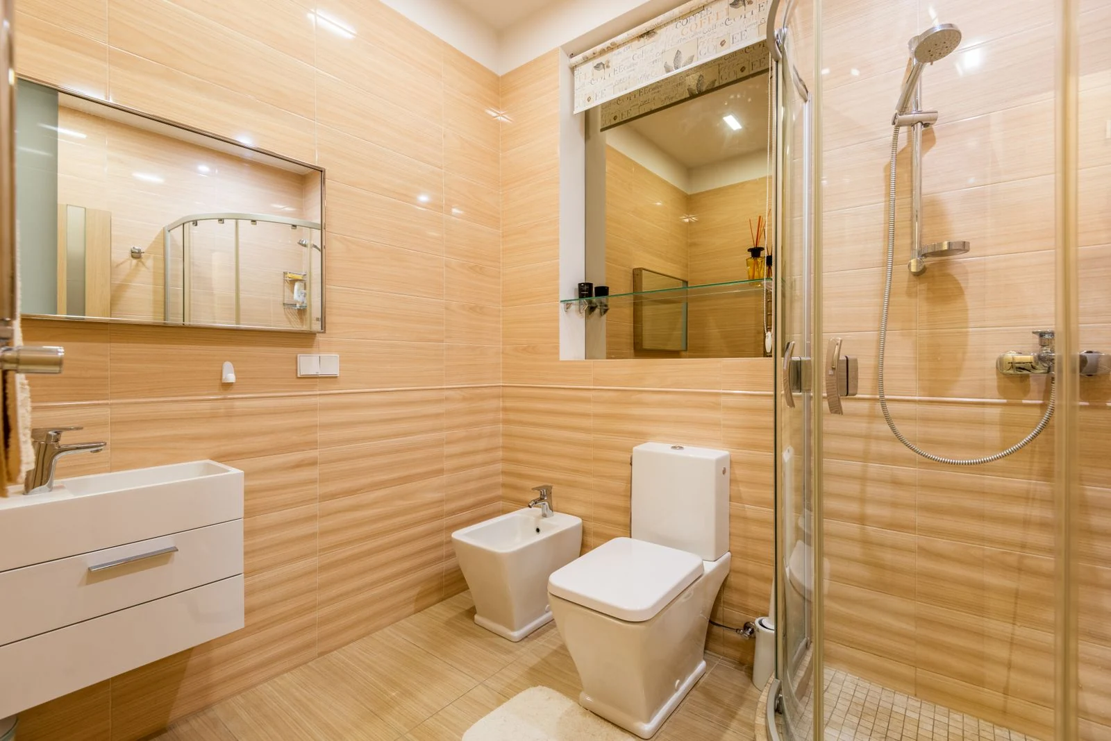 Interior of modern bathroom with light orange walls and white sink under mirror near toilet and bidet next to shower cabin