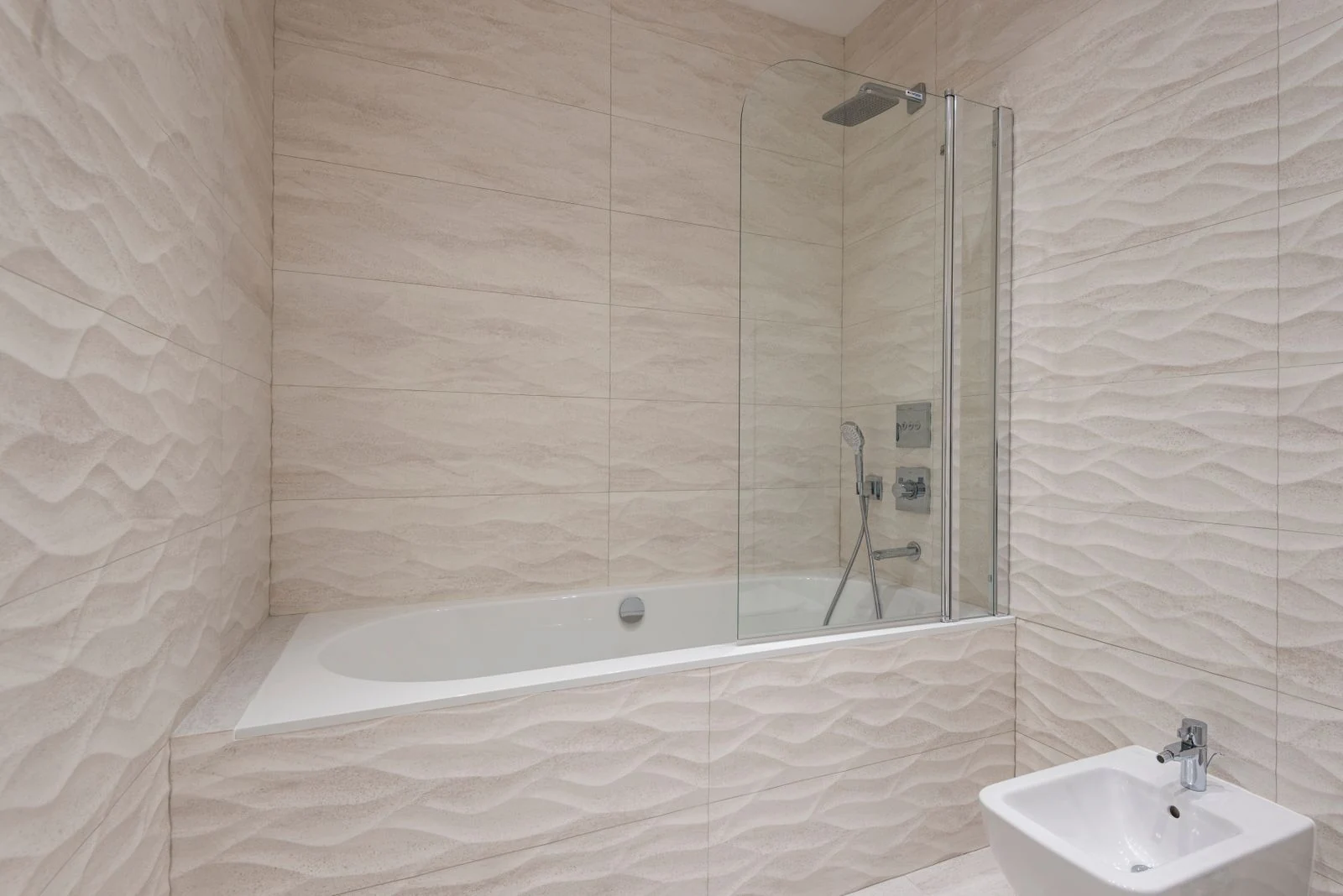 A sleek modern bathroom featuring a bathtub, shower, and beige textured tiles