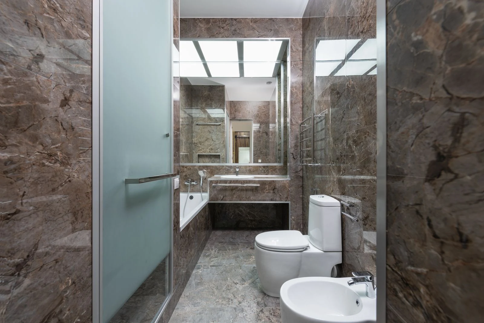 Spacious bathroom with marble walls, glass door, and modern fixtures, featuring a sink and toilet